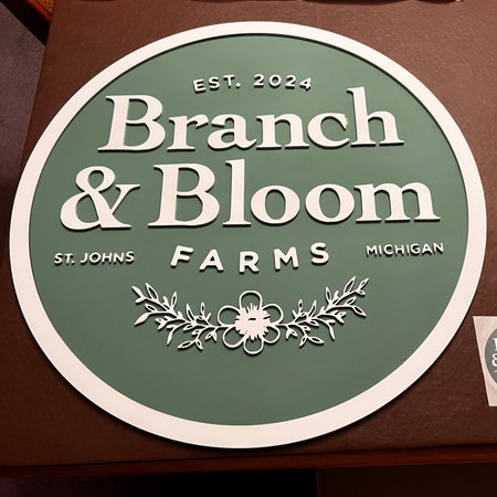 Round sign with 'Branch & Bloom Farms' branding on a brown surface